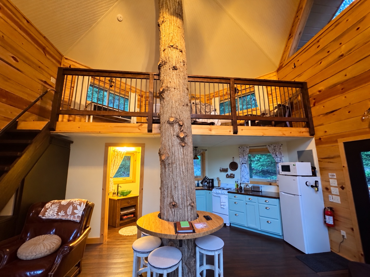 Treehouse interior with a cedar trunk rising through the round table beneath the loft